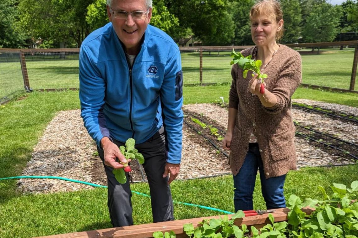 Two gardeners proudly holding freshly harvested radishes in front of the community garden at First Presbyterian Church