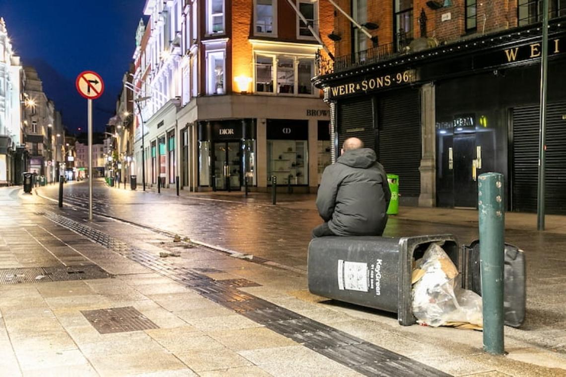 A lone man sits in an empty city street during a severe winter storm. His isolation mirrors the human cost of inaction, as extreme weather and inequality grow side by side.
